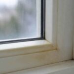 Zabrudzona biała rama okienna i parapet z widocznymi śladami osadu przy szybie